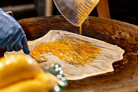 Roti. Close-up of beaten eggs poured onto dough in process of preparing sweet dessert on heated surface. Vibrant colors enhance delicious appearance and convey careful preparation of street foodの写真素材