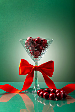 Decorative glass filled with red necklace, adorned with vibrant red bow, set against green background. Perfect for festive, celebratory and holiday designsの写真素材