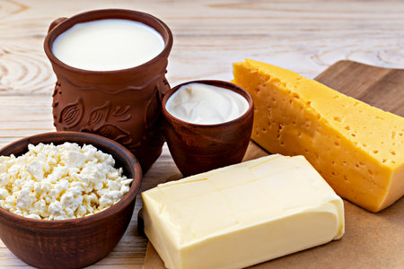 Various dairy products, including milk in rustic clay jug, cottage cheese, butter, sour cream and slice of yellow cheese, arranged on wooden table. Fresh and traditional farm-style dairy selectionの写真素材