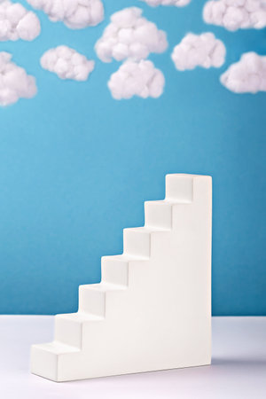 Minimalist white staircase against blue background with fluffy cotton clouds. Surreal and conceptual representation of progress, elevation and dreams. Ideal for creative and motivational themesの写真素材
