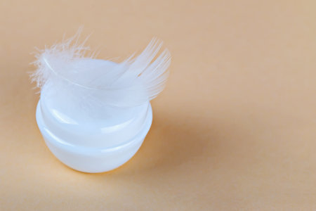 Mockup. Cream jar with feather symbolizes gentle skincare on pastel background. Cream for delicate skin treatment and luxury beauty routines. Cosmetic cream represents softness skincare trendの写真素材