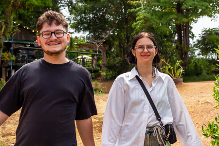 Young couple smiling and walking together outdoors, surrounded by greenery, enjoying sunny day,...