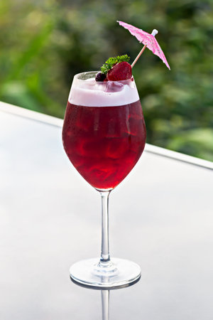 Refreshing cocktail served in stylish glass, garnished with pink umbrella and fresh berries, set against blurred natural background, perfect for summer gatherings and celebrations. Verticallyの写真素材