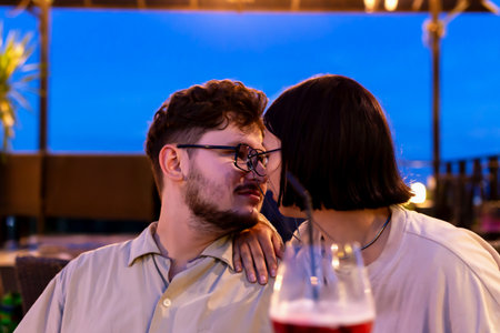 Romantic date on restaurant terrace at sunset. Romantic couple enjoying tender moment together at sunset, surrounded by cozy outdoor atmosphere, with drinks and evening sky creating warm ambianceの写真素材