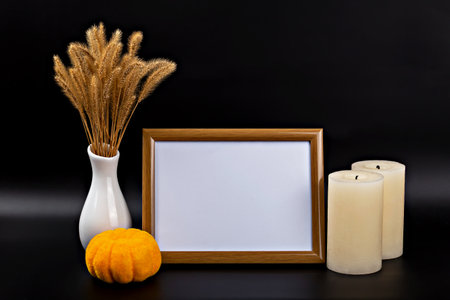 Halloween. Mockup. Autumn themed display features an empty wooden frame, decorative pumpkin, two candles and dried grass in white vase, creating warm and inviting atmosphere for seasonal decorの写真素材