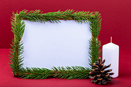 Mockup. Christmas. Festive mockup featuring blank white space for design or advertising surrounded by lush pine branches, white candle and pine cone, creating warm holiday atmosphereの写真素材