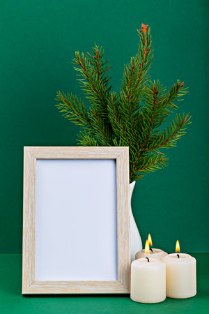 Mockup. Christmas. Decorative arrangement featuring an empty wooden frame, lit candles, and fresh evergreen branches, creating cozy and inviting atmosphere perfect for seasonal decor. Verticallyの写真素材