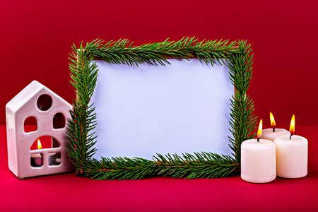 Christmas. New Year. Festive holiday frame adorned with fresh pine branches, surrounded by lit candles and charming decorative house, creating warm and inviting atmosphere for seasonal celebrationsの写真素材