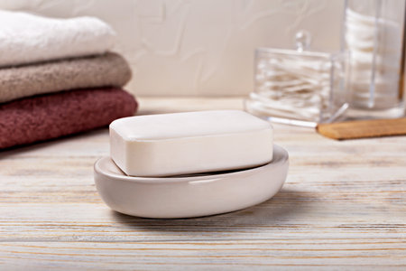Health and hygiene. White soap bar placed on smooth ceramic dish, surrounded by neatly folded towels in soft colors, creating calming atmosphere in well-organized bathroom environmentの写真素材