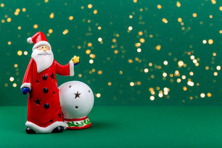 Christmas. Santa Claus. Festive Santa Claus figurine wearing red coat stands beside decorative snow globe on vibrant green background, creating cheerful holiday atmosphere with sparkling bokeh lightsの写真素材