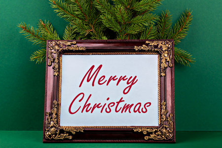 Merry Christmas. Decorative frame featuring Merry Christmas message surrounded by lush evergreen branches, set against vibrant green background, creating cheerful holiday atmosphere for celebrationsの写真素材
