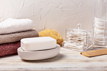 Health and hygiene. White soap bar elegantly positioned on dish, accompanied by neatly stacked towels and bathroom accessories, creating serene atmosphere for relaxation and self-careの写真素材