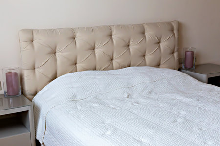 Bedroom interior. Elegant bedroom showcasing beige headboard with tufted design, complemented by cozy white bedspread and soft ambient lighting, creating serene and inviting atmosphere for relaxationの写真素材