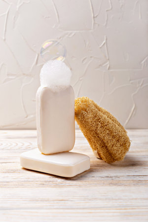 Health and hygiene. Minimalist soap display featuring two bars of soap, one with bubble and natural sponge, arranged on wooden surface, creating serene atmosphere for skincare and relaxationの写真素材