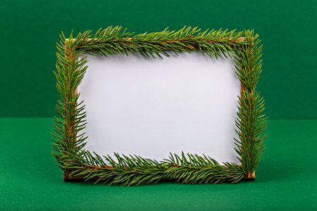 Mockup. Christmas. Blank frame adorned with fresh green pine branches, set against vibrant green backdrop, creating festive and natural atmosphere perfect for seasonal displays or invitationsの写真素材