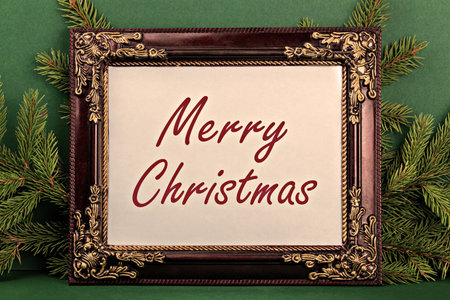 Merry Christmas. Elegant frame showcases festive message, surrounded by lush pine branches against rich green background, creating warm and inviting holiday atmosphere for seasonal celebrationsの写真素材