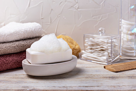 Health and hygiene. Soap bar with foam placed on dish, surrounded by neatly stacked towels and cotton swabs, creating calming atmosphere in bathroom, emphasizing cleanliness and relaxationの写真素材