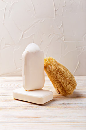 Health and hygiene. Natural soap bars stacked beside loofah sponge on wooden surface, creating serene and inviting atmosphere, showcasing organic textures and materials for calming bathroom aestheticの写真素材