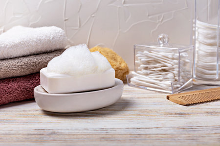 Health and hygiene. White soap bar with foam placed on dish, surrounded by soft towels and grooming accessories, creating tranquil bathroom atmosphere that emphasizes relaxation and self-careの写真素材