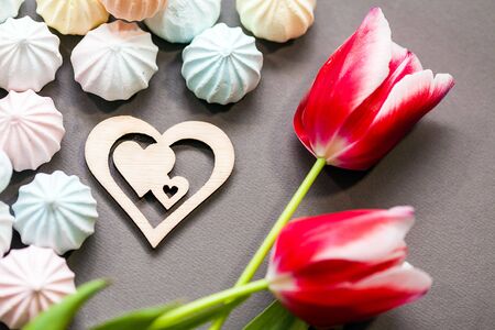meringues in pastel colors with wooden figure of heart and three red tulips on grey background.の写真素材