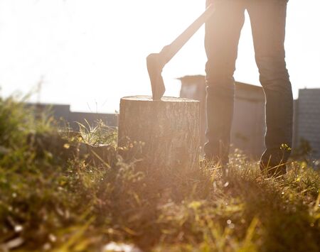 Man in jeans and shirt holding old axe on the stump.の写真素材