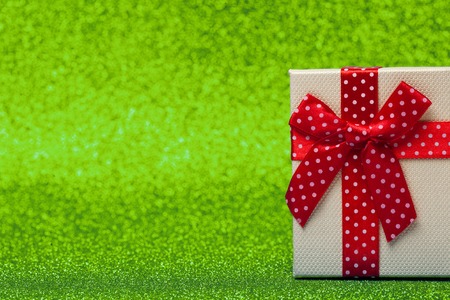 Gift box with red bow on sparkling green background. Bright and festive.の写真素材