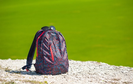 backpack on white rock on green fresh drass background. Sunny gay travelling concept. Place for text.の写真素材