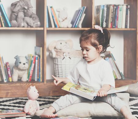 Cute emotional little girl reading book to her toyの写真素材