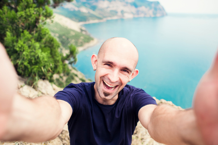 Young man taking travel selfie on trekking excursion day - Hipster guy self photo at view point with blue ocean background - Concept of healthy lifestyle in beauty of nature.の写真素材