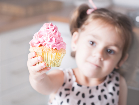 Cute little girl holding birthday cupcakes in kitchen. Festive and holiday conceptの写真素材