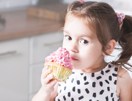 Cute little girl holding birthday cupcakes in kitchen. Festive and holiday conceptの写真素材