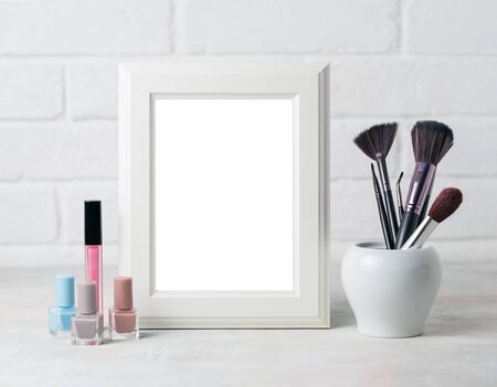 White wooden frame with copyspace and cosmetic brushesh and nail polish. Fahion beauty mockup concept on white Brick wall background.の写真素材