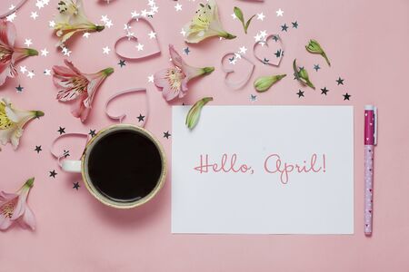 Cup of coffe and spring greeting with a pen, flower composition and words Hello April on pink background. top view, flat layの写真素材