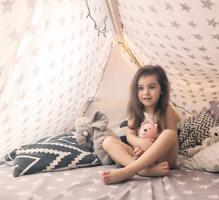 Cute happy little girl playing with toys and dreaming in teepee and bed. Close up photo of happy childの写真素材