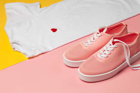Top view of white woman t-shirt and pink shoes on pink and yellow background. Fashion clothes set....