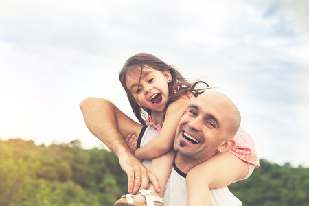 Little girl sitting on father's shoulders and laughing. Summer day, happy family and summer lifestyle conceptの写真素材