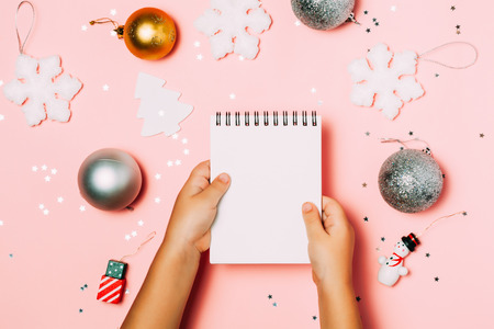 Child's hands holding empty note boo in hands on sparkling pink background with christmas accessories.の写真素材