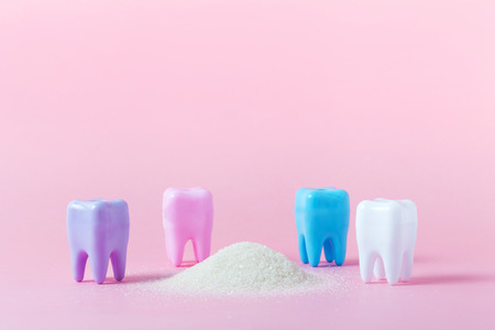 Plastic tooth and toothbrush in big pile of sugar. Caries and sugar concept. Dental care concept on...