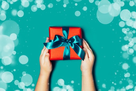 Child hands holding beautiful gift box on blue background, with sparkling glitter around. Holiday, bright and festive view, flat lay. Copy space for text. Christmas greeting banner.の写真素材