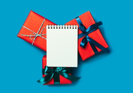 Minimalistic Christmas gift boxes wrapped in red paper and empty notebook on turquoise background. Bright and festive Christmas concept. Top view, flat lay. Copy space for text.の写真素材