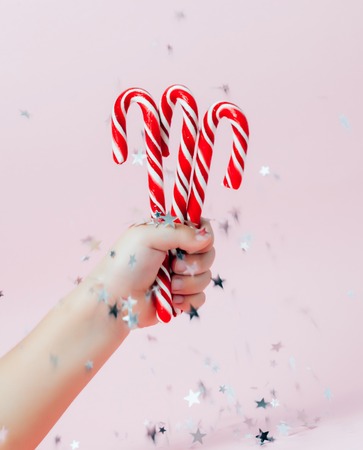 Child's hand holding christmas candies on pink festive and sparkling background. Minimalist christmas concept.の写真素材