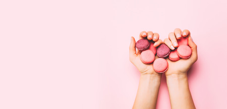 Beautiful female hands with trendy manicure holding pink macaroon cake. Top view, flat lay. Copyspace for your text.の写真素材