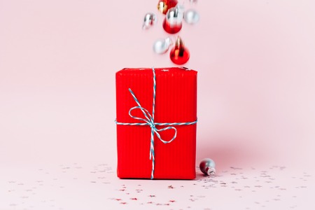 Christmas gift box wrapped in red paper on festive pink background. Stars and shiny glitter falling...