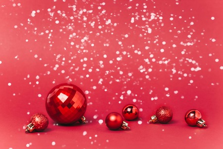 Christmas red background with christmas balls and snow falling on them. Christmas festive concept.