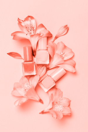 Flowers and nail poloshes composition on Living Coral table Beauty and manicure concept. Top view, flat lay. Color of the year 2019.の写真素材