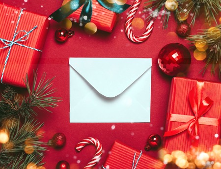 Christmas red background with christmas balls and present with candies and snow falling on them and an the envelope. Christmas festive greeting concept. Copy space for text.の写真素材