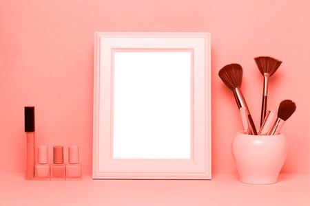 Mock up frame and nail polishes with make up brushes and accessorises women's table with Living coral background. Color of the year 2019 concept.の写真素材