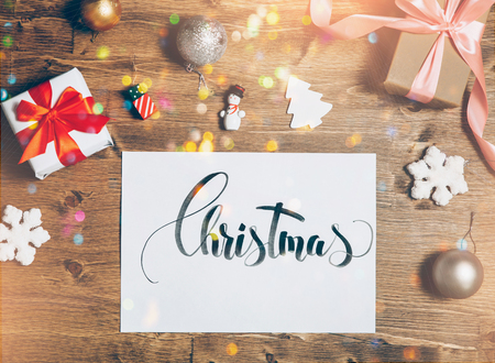 Christmas lettering card on wooden table with holiday box and different accessorieses. Bright and festive. Vintage look. Top view, flat lay.の写真素材