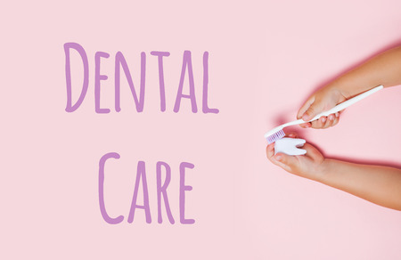 Child's hands holding big tooth and toothbrush on pink backgroubd. Healty care teeth concept. Top view, flat lay. Dental care text.の写真素材