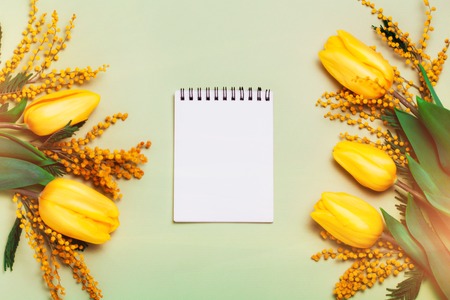 Pink tulips and mimosa flowers on green trendy background. Empty notebook for your text. Spring greetings. Flat lay, top viewの写真素材